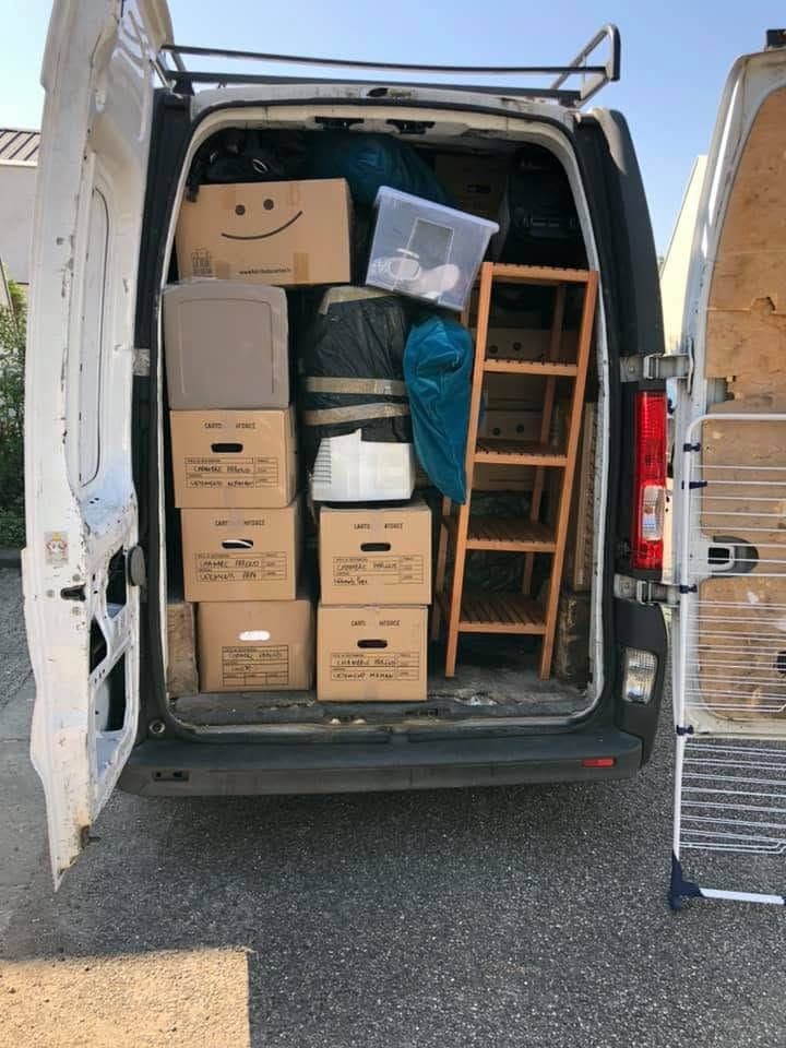 Arrière d'un utilitaire ouvert, chargé jusqu'au plafond : cartons étiquetés à la main pièce par pièce, empilés et calés du plancher au toit, avec une étagère glissée le long de la paroi.